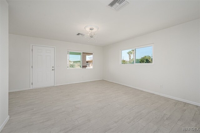 unfurnished room with an inviting chandelier, light wood-type flooring, visible vents, and baseboards