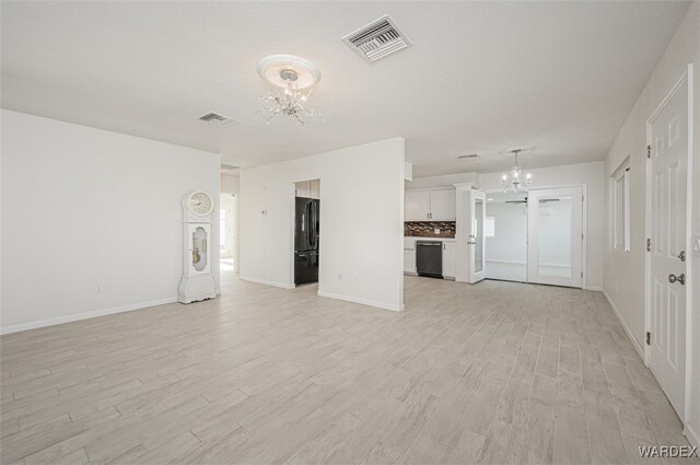 unfurnished living room with a chandelier, baseboards, visible vents, and light wood-style floors