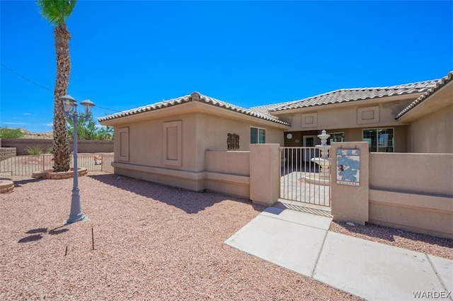 view of front of property featuring a fenced front yard, a gate, a tile roof, and stucco siding