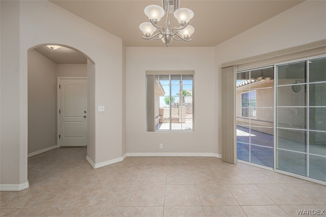 spare room featuring arched walkways, a notable chandelier, baseboards, and light tile patterned floors