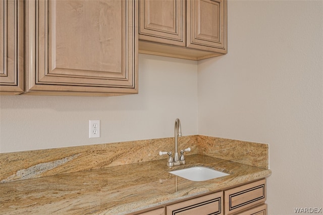 kitchen featuring light stone counters, light brown cabinets, and a sink