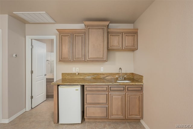 kitchen featuring light stone counters, refrigerator, visible vents, a sink, and baseboards