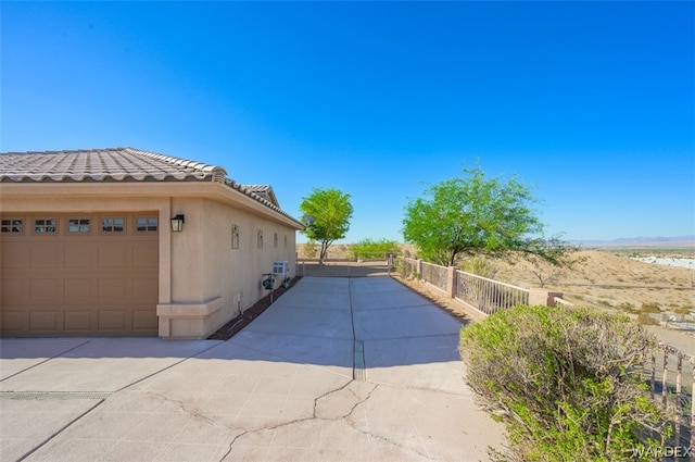 view of property exterior with a garage, concrete driveway, a tile roof, fence, and stucco siding