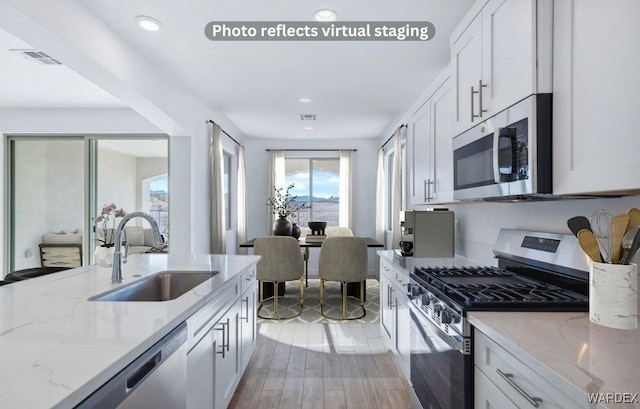 kitchen featuring stainless steel appliances, visible vents, white cabinets, a sink, and light stone countertops