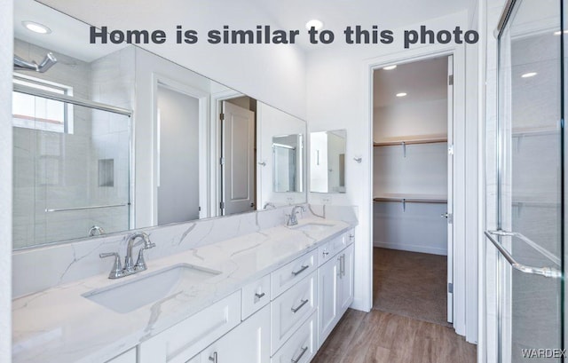 bathroom with a stall shower, a spacious closet, a sink, and wood finished floors