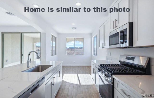 kitchen with stainless steel appliances, white cabinetry, a sink, and light stone counters