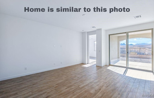 spare room with wood finished floors, visible vents, and baseboards