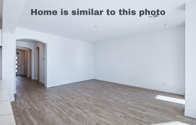 unfurnished room featuring arched walkways, light wood-type flooring, visible vents, and baseboards