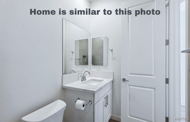 half bathroom with a textured wall, vanity, and toilet