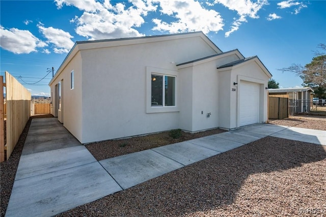view of property exterior featuring an attached garage, fence, driveway, and stucco siding