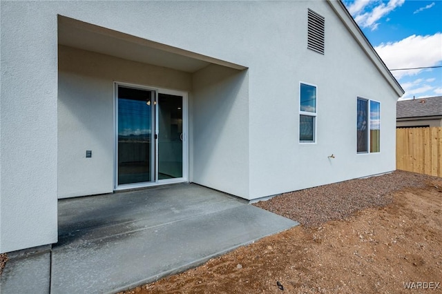 rear view of property featuring a patio area, fence, and stucco siding