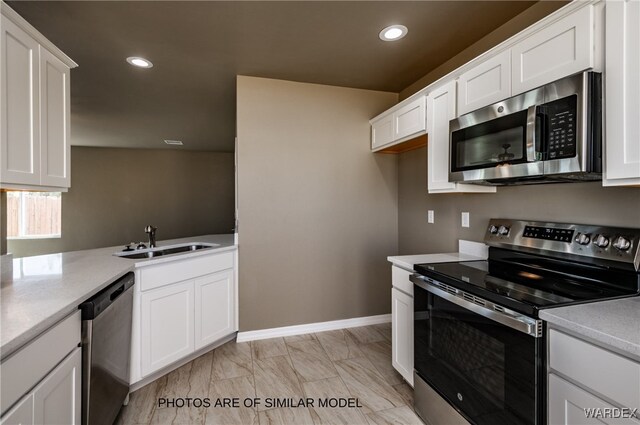 kitchen with white cabinets, stainless steel appliances, light countertops, a sink, and recessed lighting