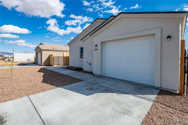 view of side of home with fence, an attached garage, stucco siding, concrete driveway, and an outdoor structure