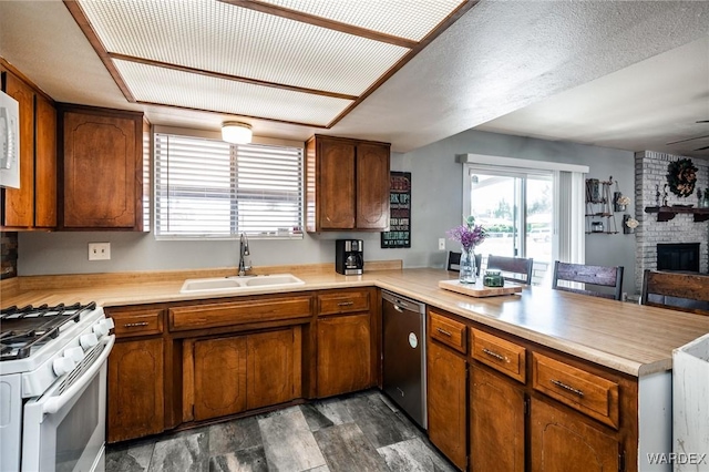 kitchen featuring light countertops, a brick fireplace, a sink, white appliances, and a peninsula