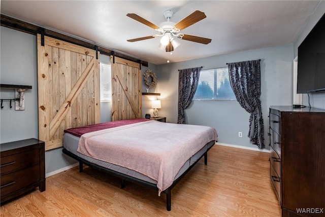 bedroom with a barn door, light wood-type flooring, and baseboards