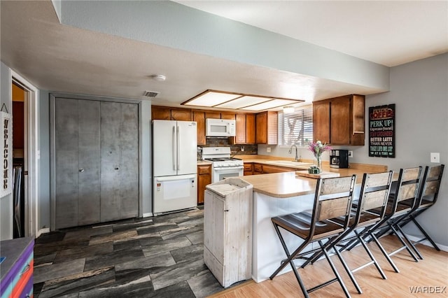 kitchen with a breakfast bar area, light countertops, a sink, white appliances, and a peninsula