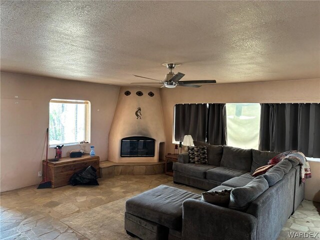 living area featuring a ceiling fan, a large fireplace, and a textured ceiling