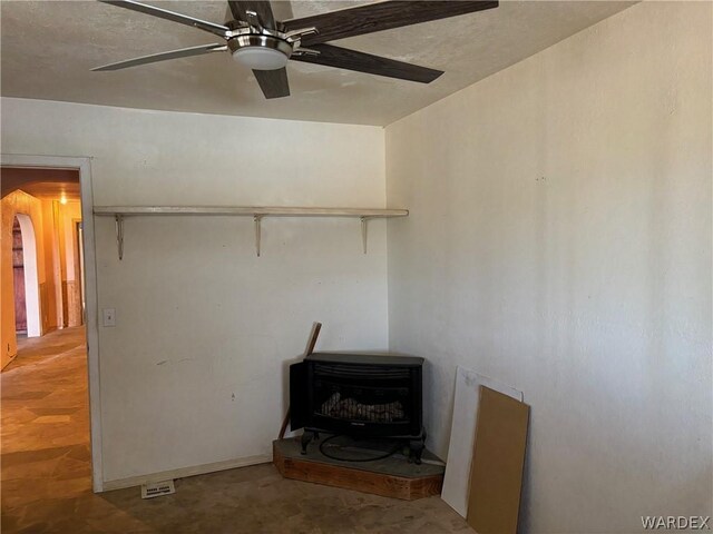 unfurnished living room featuring arched walkways, ceiling fan, concrete floors, and a wood stove