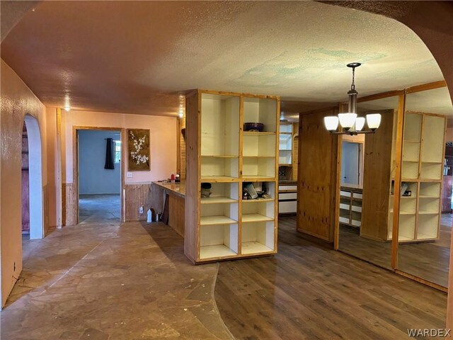 interior space featuring a chandelier, arched walkways, a textured ceiling, and wood finished floors