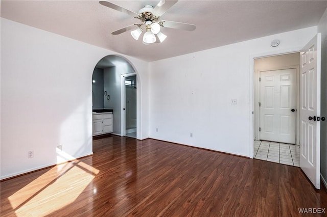 empty room featuring ceiling fan, baseboards, arched walkways, and wood finished floors