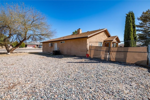 view of side of property with stucco siding, a wall unit AC, a chimney, and fence