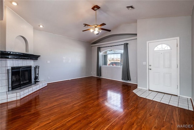 unfurnished living room with visible vents, a tiled fireplace, a ceiling fan, wood finished floors, and vaulted ceiling