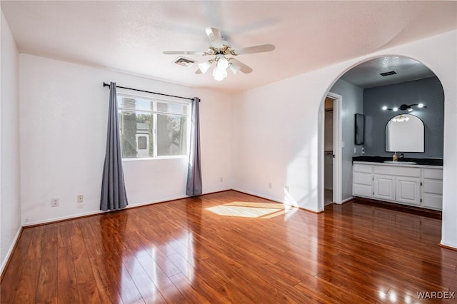 spare room with dark wood-style floors, visible vents, arched walkways, ceiling fan, and a sink