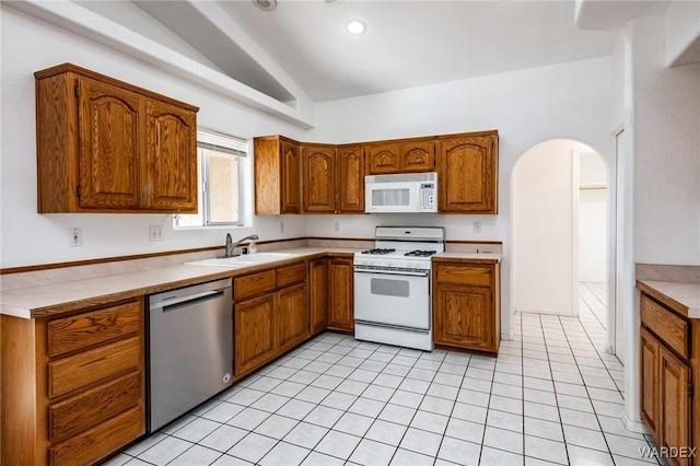 kitchen featuring white appliances, brown cabinetry, arched walkways, a sink, and vaulted ceiling