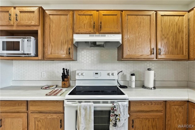 kitchen featuring white appliances, light countertops, under cabinet range hood, and backsplash