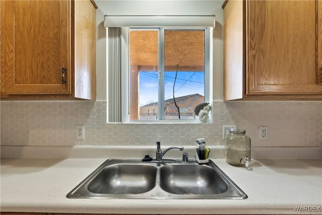 kitchen featuring backsplash, light countertops, a sink, and brown cabinetry