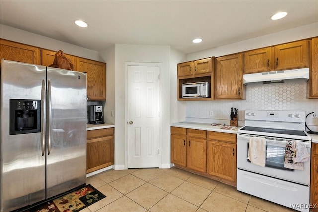 kitchen with light tile patterned floors, under cabinet range hood, light countertops, appliances with stainless steel finishes, and brown cabinetry