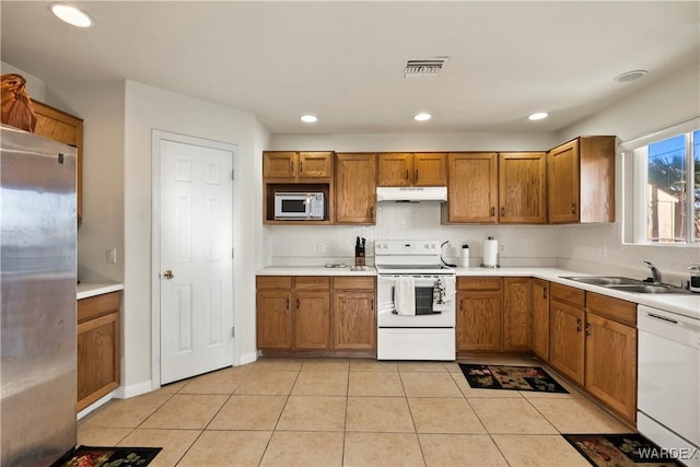 kitchen with brown cabinetry, white appliances, light countertops, and under cabinet range hood