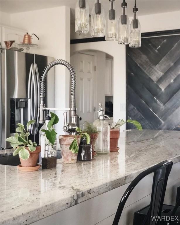 interior space with light stone counters, decorative light fixtures, a dry bar, and stainless steel fridge with ice dispenser