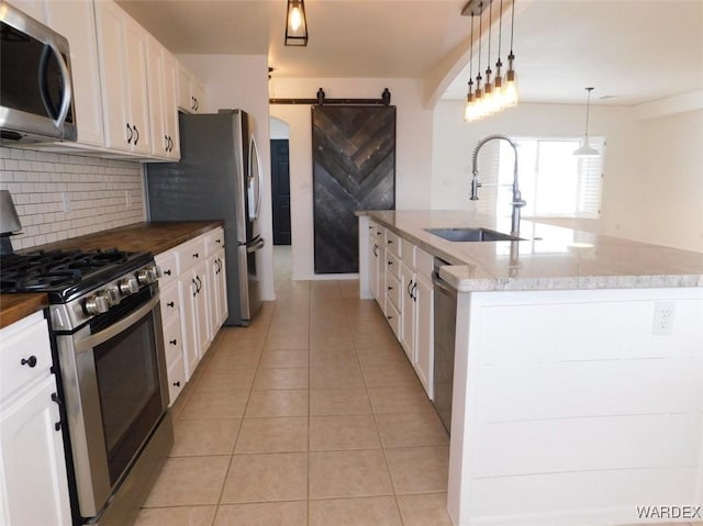 kitchen with light tile patterned floors, a barn door, stainless steel appliances, a sink, and white cabinets