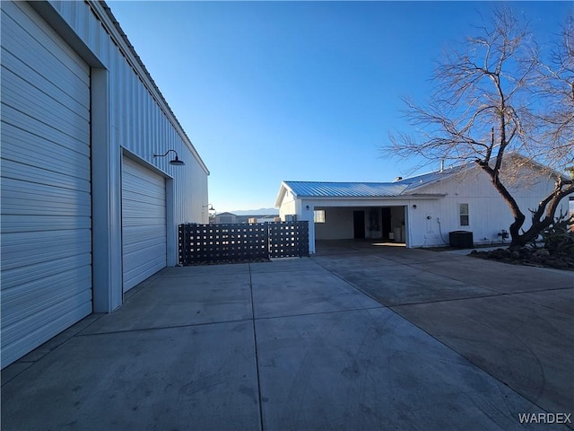 view of property exterior featuring a garage, concrete driveway, central AC unit, and metal roof