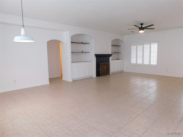 unfurnished living room featuring built in shelves, light tile patterned floors, and a ceiling fan