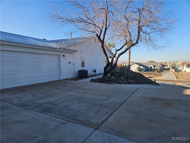 view of side of property featuring metal roof, concrete driveway, an attached garage, and cooling unit