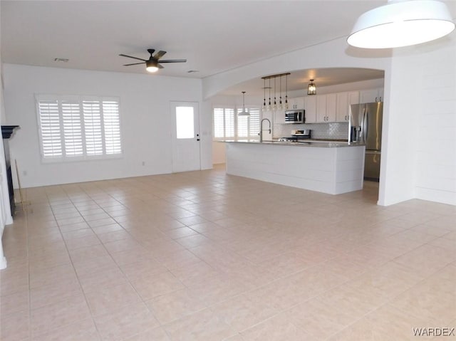 unfurnished living room featuring light tile patterned floors, arched walkways, a sink, visible vents, and a ceiling fan