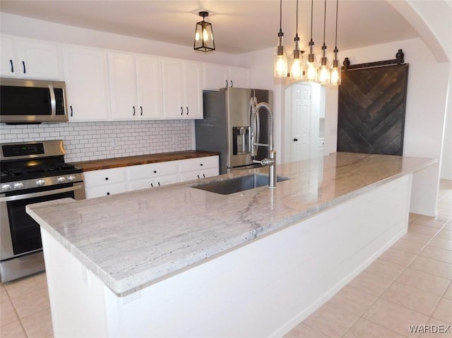 kitchen featuring light tile patterned floors, light stone counters, white cabinets, appliances with stainless steel finishes, and decorative backsplash