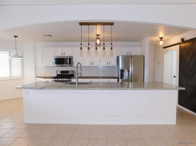 kitchen featuring a barn door, a sink, appliances with stainless steel finishes, and decorative backsplash