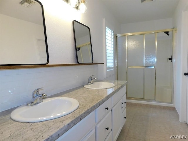 full bathroom with double vanity, a stall shower, visible vents, and a sink