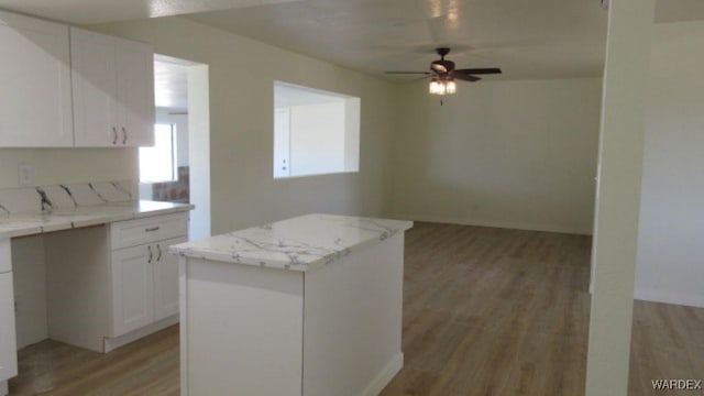 kitchen with white cabinetry, a ceiling fan, baseboards, a kitchen island, and light wood-style flooring