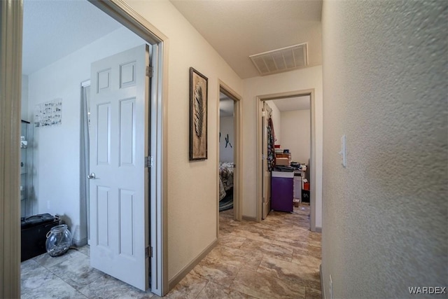 hallway with a textured wall, visible vents, and baseboards