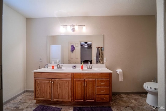 bathroom featuring baseboards, a sink, toilet, and double vanity