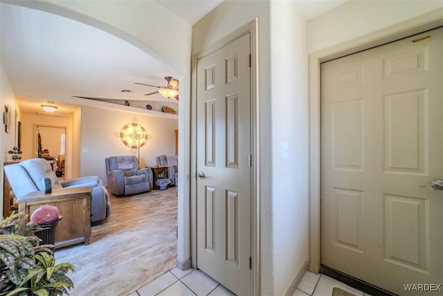 hallway with arched walkways, light tile patterned floors, and baseboards