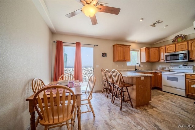 kitchen with stainless steel microwave, light countertops, brown cabinetry, white range with electric cooktop, and a kitchen bar