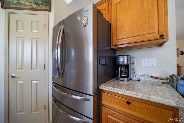 kitchen featuring brown cabinetry, stainless steel refrigerator with ice dispenser, and light stone counters