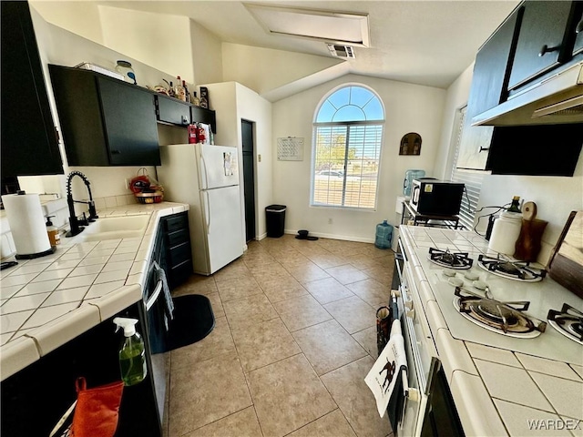 kitchen featuring tile counters, lofted ceiling, visible vents, white appliances, and dark cabinetry