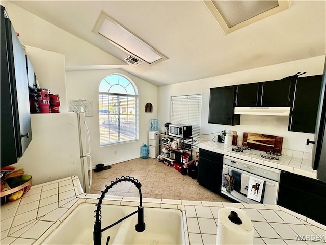 kitchen featuring white appliances, visible vents, vaulted ceiling, dark cabinetry, and under cabinet range hood