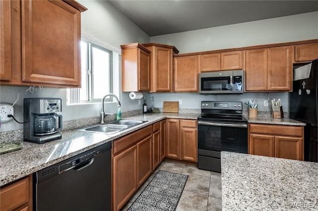 kitchen featuring light tile patterned floors, brown cabinetry, light stone countertops, black appliances, and a sink